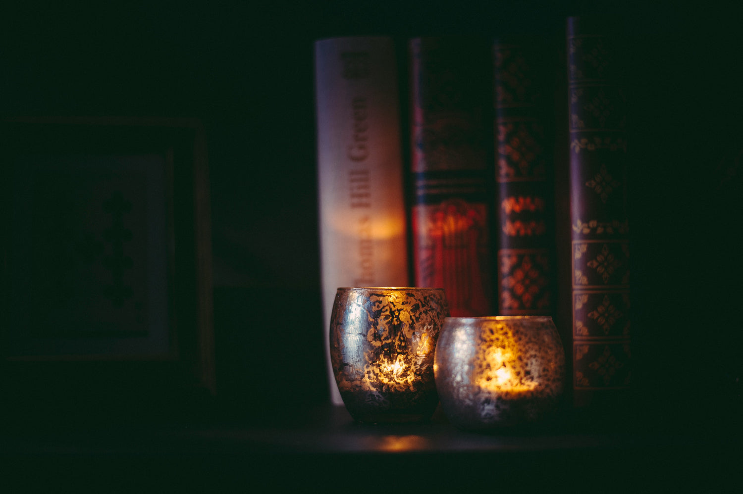 Two lit candle holders with books in the background on a dark surface