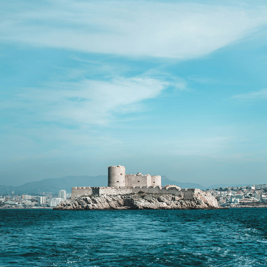 Castle on a small island in the middle of a body of water with a city skyline in the background.