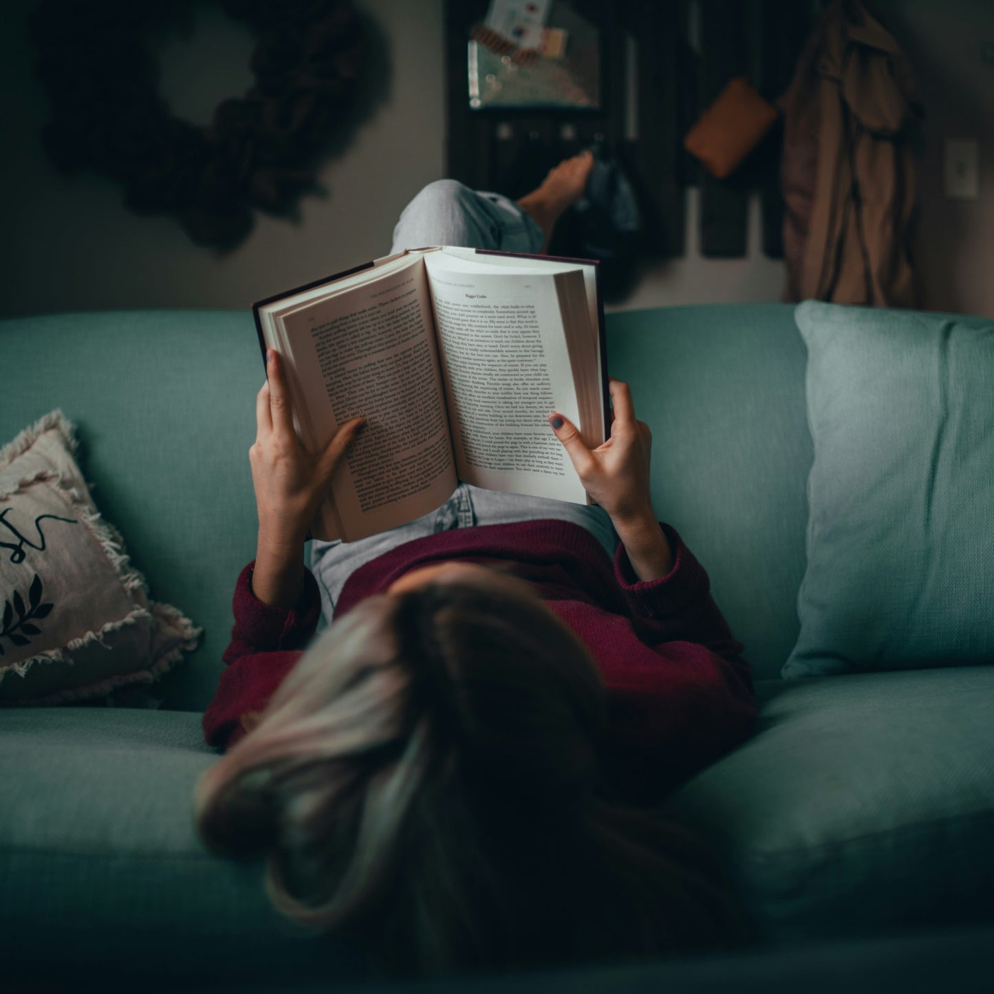 Person reading a book on a teal couch in a cozy living room.