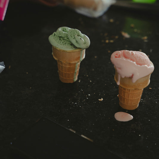 Two small ice cream cone models on a dark surface with a blurred background.