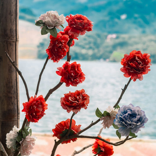 Decorative floral branch with red and blue flowers against a scenic background of water and mountains.