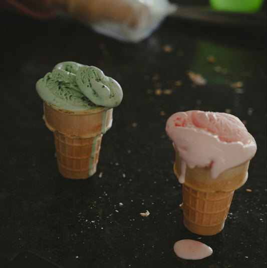 Two small ice cream cone models on a dark surface with a blurred background.
