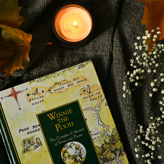 Book titled 'Winnie the Pooh' with a candle and flowers on a textured surface